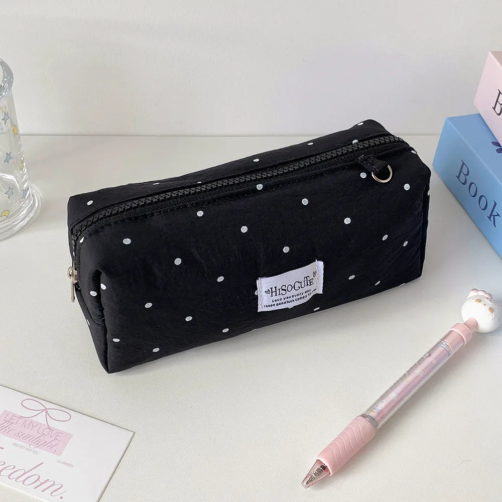 Eine schwarze Polka-Dot-Pencilcase neben einem rosa Bleistift und einem blauen Buch
