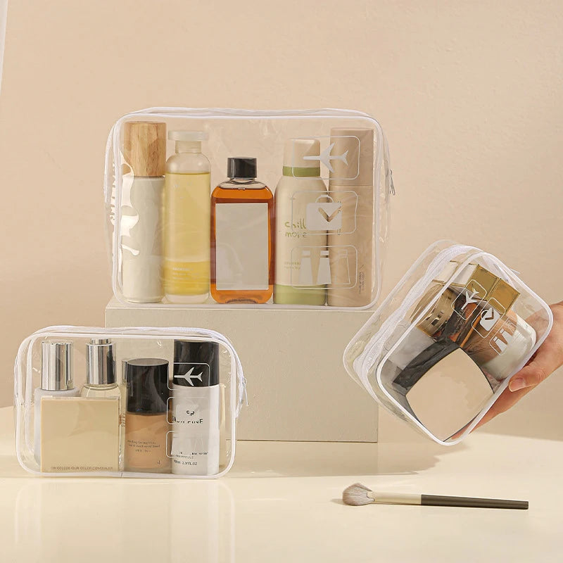 A clear PVC toiletry bag holds various skincare and cosmetic bottles and tubes on a white surface.