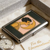 A silver metal card holder featuring an Art Deco illustration of a woman kissing the moon on a pink background.