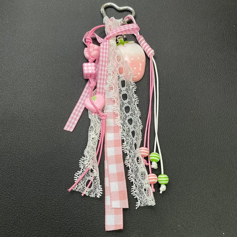 A pink and white checkered fabric bag charm keychain featuring a strawberry-shaped charm and dangling pink and green beads.