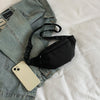 Un sac bandoulière en nylon noir est posé sur une veste en jean gris clair et un chemisier blanc.