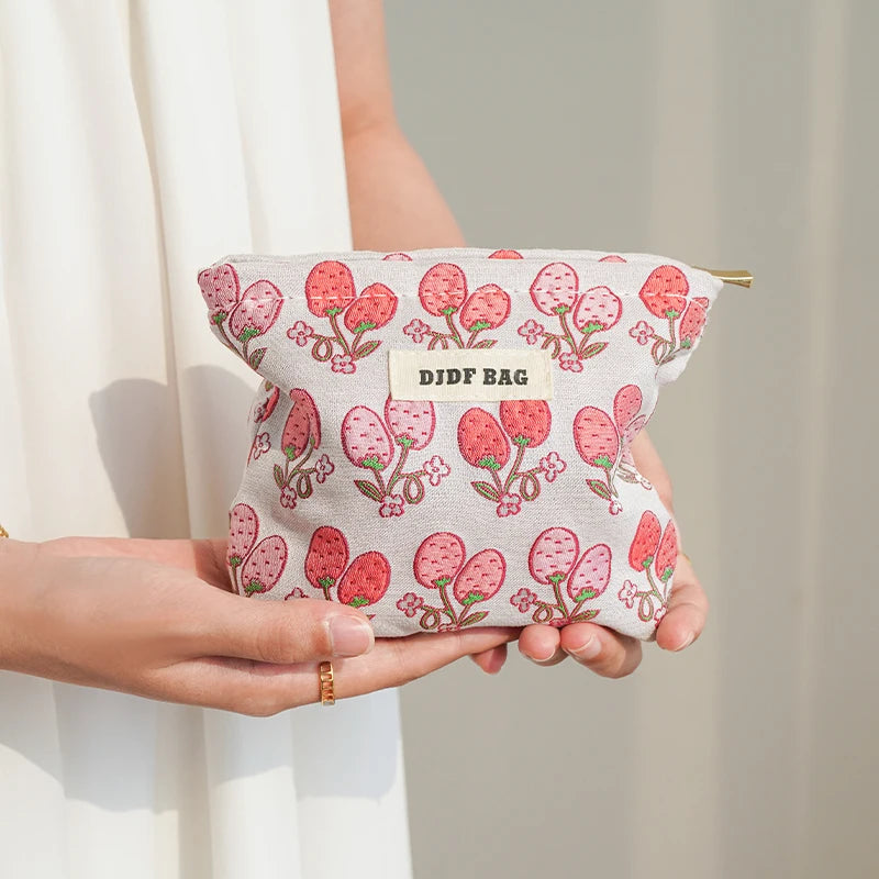 A hand holds a pink floral canvas makeup bag with the text DIDF BAG on it.
