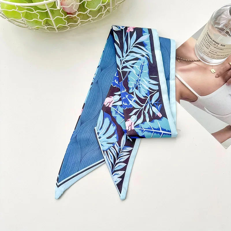 Foulard floral en soie bleu et violet plié, exposé sur une surface blanche.