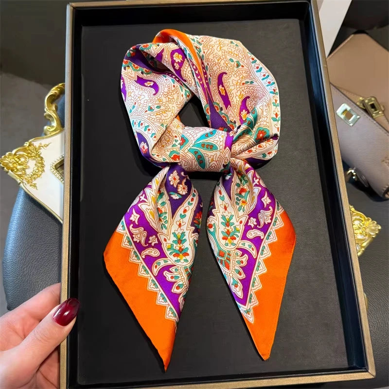 A silk paisley scarf in orange and purple is displayed on a black tray.