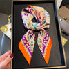 A silk paisley scarf in orange and purple is displayed on a black tray.