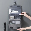 Un sac organisateur en tissu gris portable accroché au mur, montrant ses compartiments intérieurs.