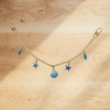 A delicate gold chain necklace with blue feather and star charms displayed on a wooden surface.