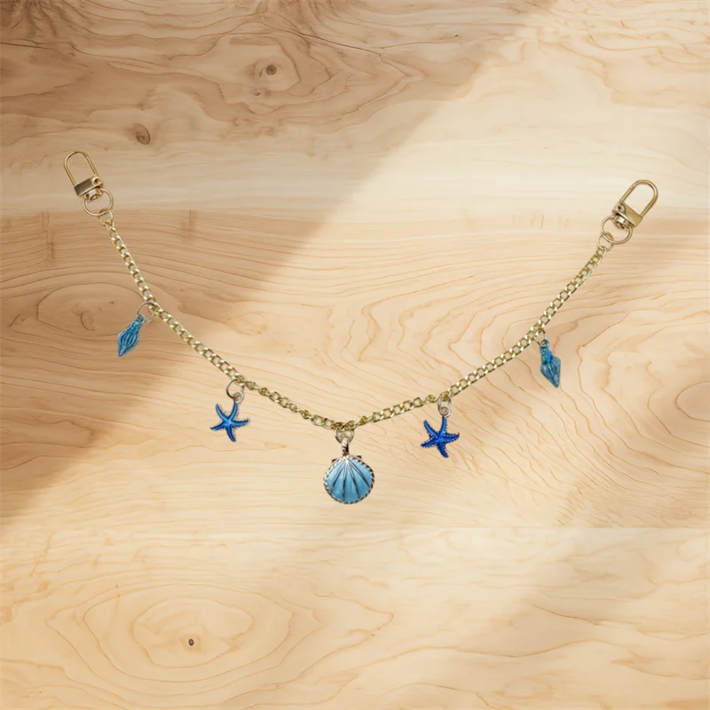 A delicate gold chain necklace with blue feather and star charms displayed on a wooden surface.