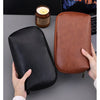 A brown leather multi-layer cable organizer pouch is shown next to a candle and a laptop.