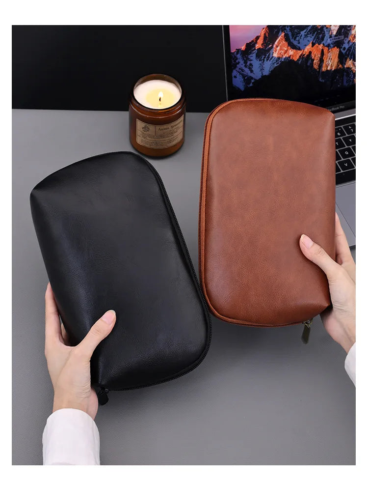 A brown leather multi-layer cable organizer pouch is shown next to a candle and a laptop.