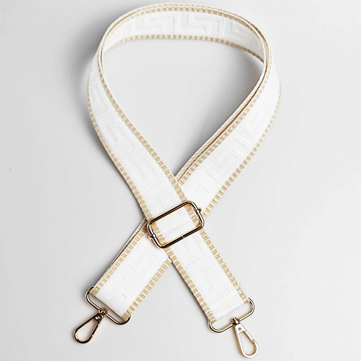 A white adjustable crossbody bag strap with a maze pattern and gold-toned hardware.