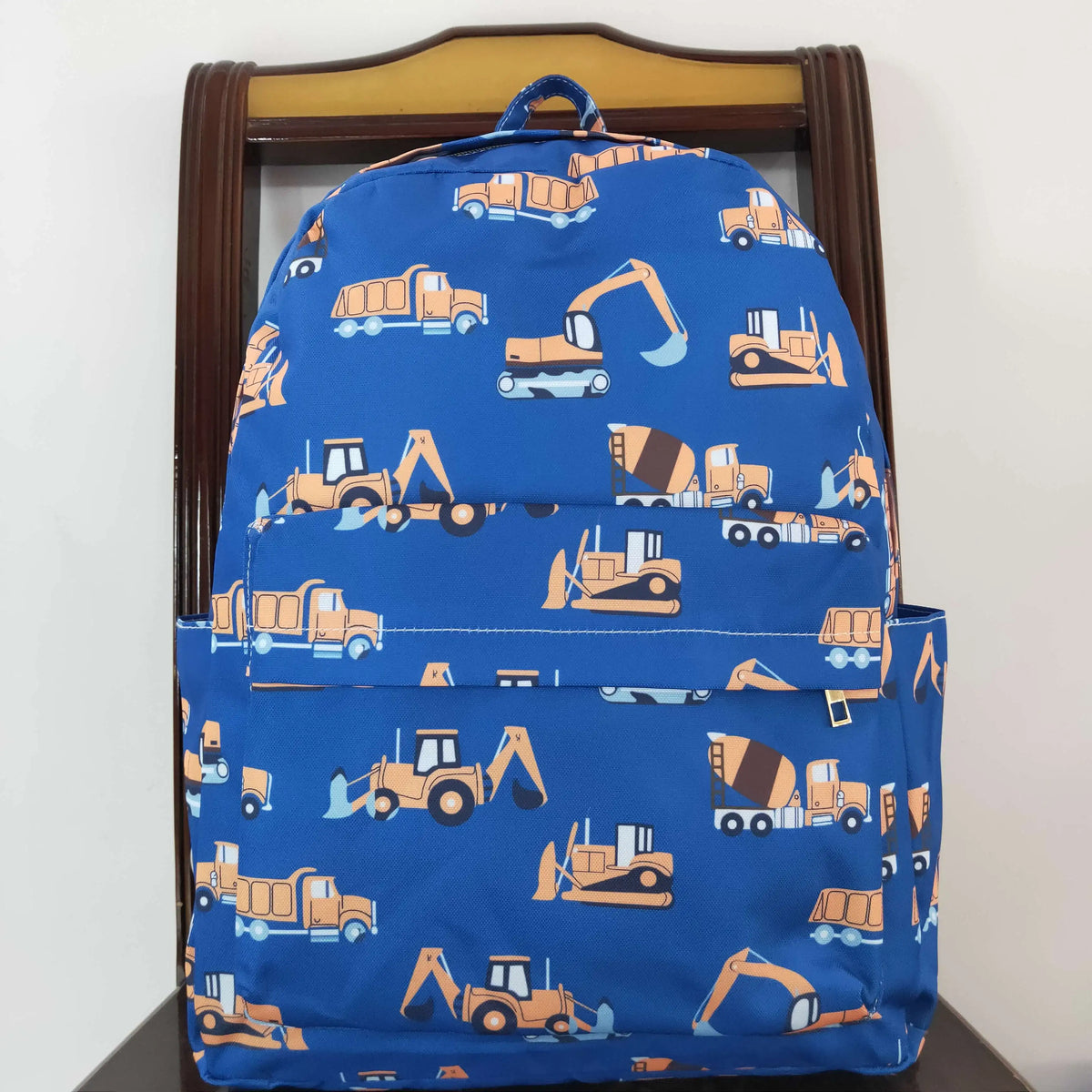 Blue backpack featuring an all-over pattern of yellow and orange construction vehicles like trucks and excavators.