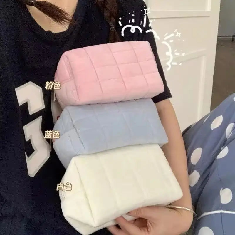 A hand holds a stack of large, quilted cosmetic storage pouches in various pastel colors.
