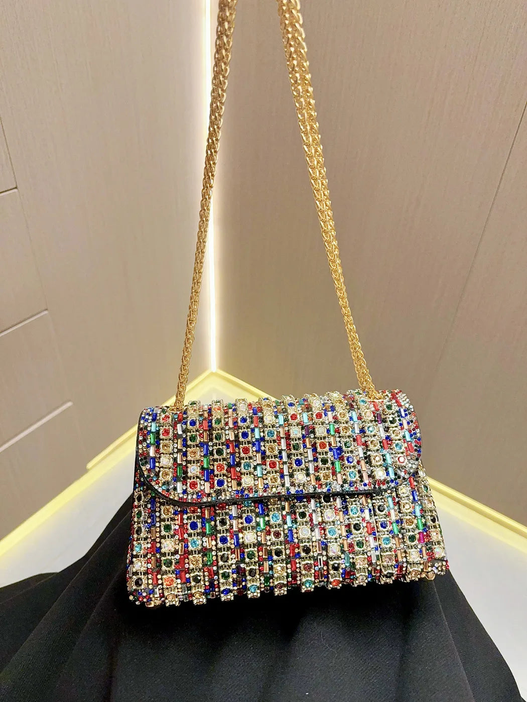 A gold chain strap holds a rectangular evening clutch bag covered in colorful rhinestones.