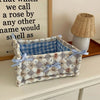 A quilted cotton storage basket with a lace flower design and light blue ribbon, sitting on a wooden surface.