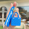 A bright blue silicone heart beach bag keychain is held in a hand against a blurred outdoor background.