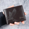 A dark brown leather wallet with an embossed eagle design is held in a person's hand.