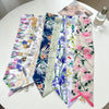 Collection de foulards pour cheveux en soie floraux élégants et colorés, disposés sur une table blanche.