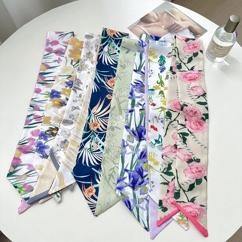Collection de foulards pour cheveux en soie floraux élégants et colorés, disposés sur une table blanche.