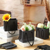 Bolsas de regalo de papel grueso negro con asas de cuerda expuestas sobre una superficie de madera.