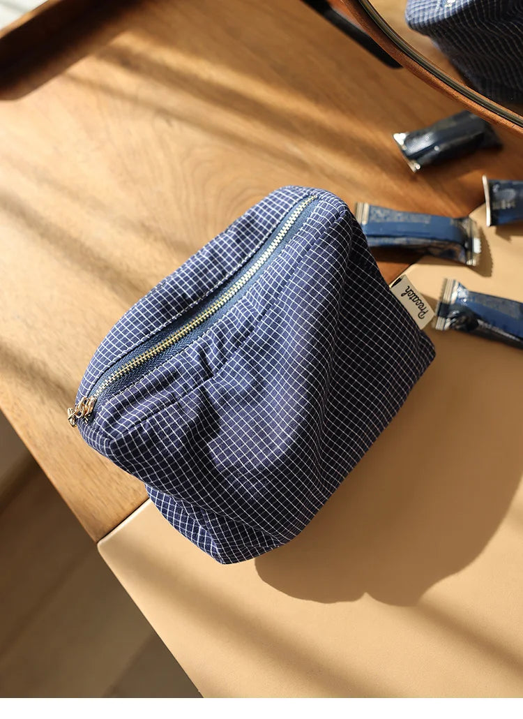 Pochette de rangement cosmétique à motif à carreaux bleu marine posée sur une surface en bois clair avec d'autres petits obje