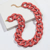 A necklace featuring a chunky, matte coral-pink acrylic chain with a gold-tone clasp, displayed on a white box.