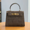 A brown leather tote bag with a crocodile pattern and gold hardware sitting on a wooden table.