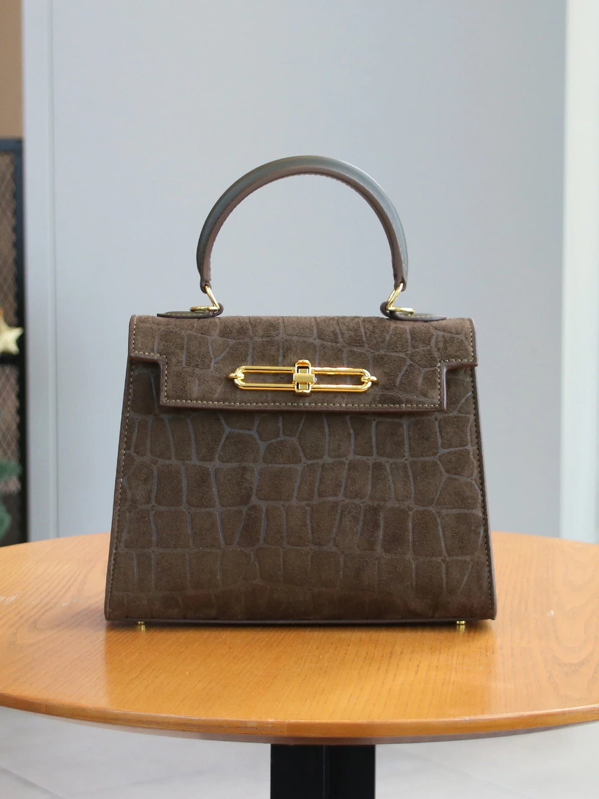 A brown leather tote bag with a crocodile pattern and gold hardware sitting on a wooden table.