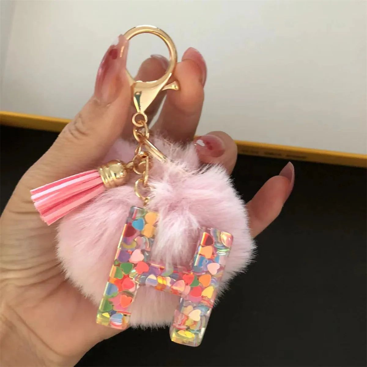 A hand holds a custom initial letter keychain featuring a shiny resin pendant and pink alphabet charm.