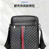 Bolso cruz de cuero negro a cuadros para hombre con rayas verdes y rojas, mostrado sobre una superficie blanca.