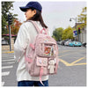 A woman wearing a white sweater and jeans carries a pink backpack on a city street.