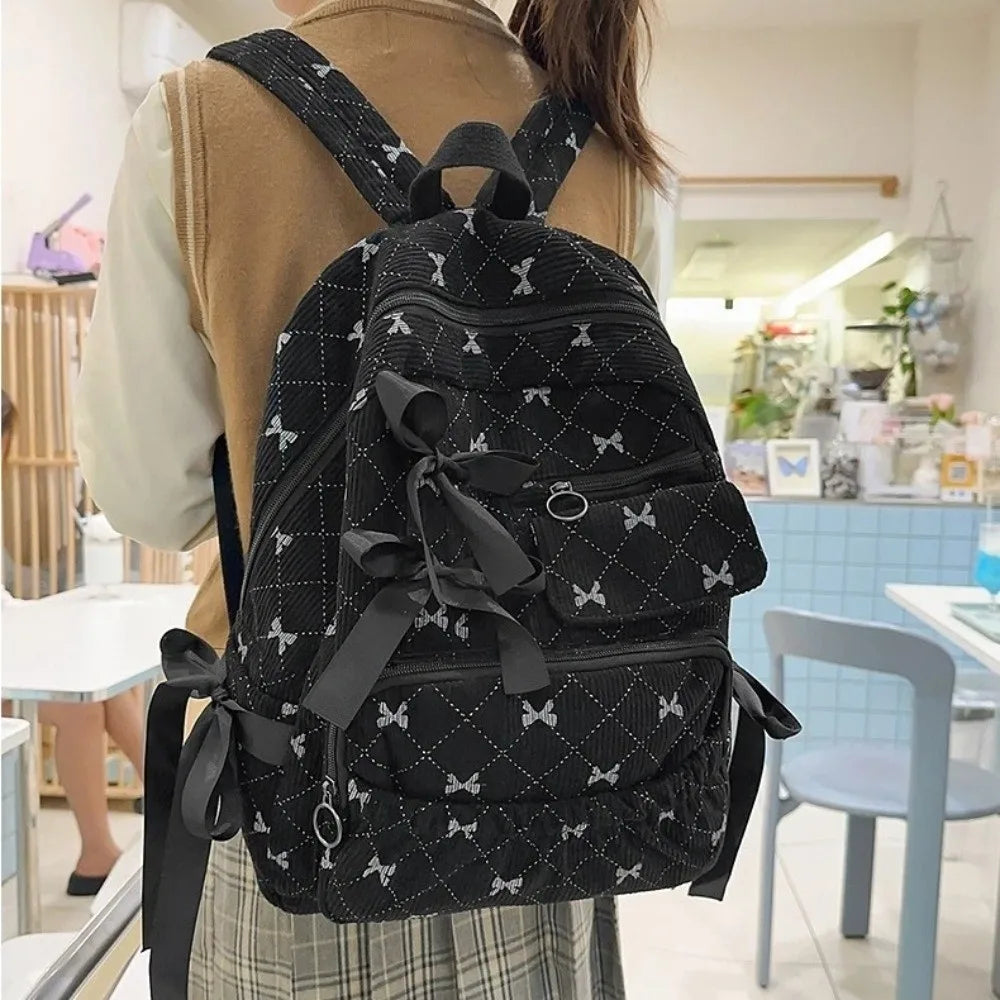 A woman is wearing a black corduroy backpack with a bow print pattern and brown jacket.