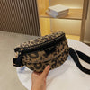 A hand holds a black and gold leopard print crossbody shoulder bag on a white surface.