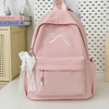 A pink embroidered backpack with a white bow and pocket on a white surface.
