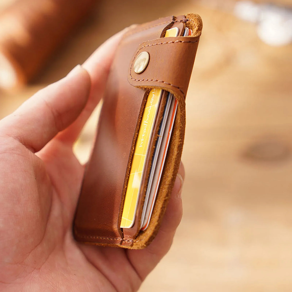 Una mano sostiene un delgado portacartas de cuero marrón genuino con una tarjeta de color dorado dentro.