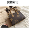 A dark brown ladies' shoulder tote bag with tan leather handles and gold hardware resting on a light beige fabric.