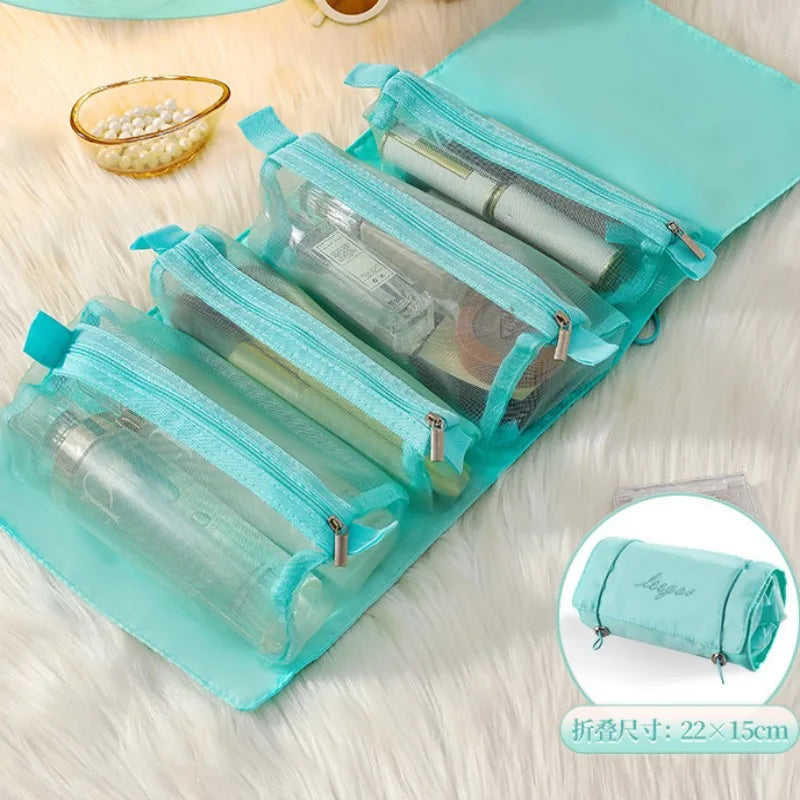 A teal portable detachable makeup bag with multiple clear zippered compartments resting on a white fluffy surface.