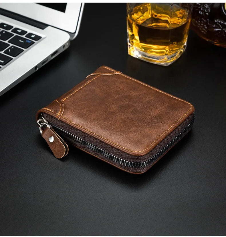 A brown retro PU leather men's wallet lying on a dark surface next to a laptop and a glass of amber liquid.