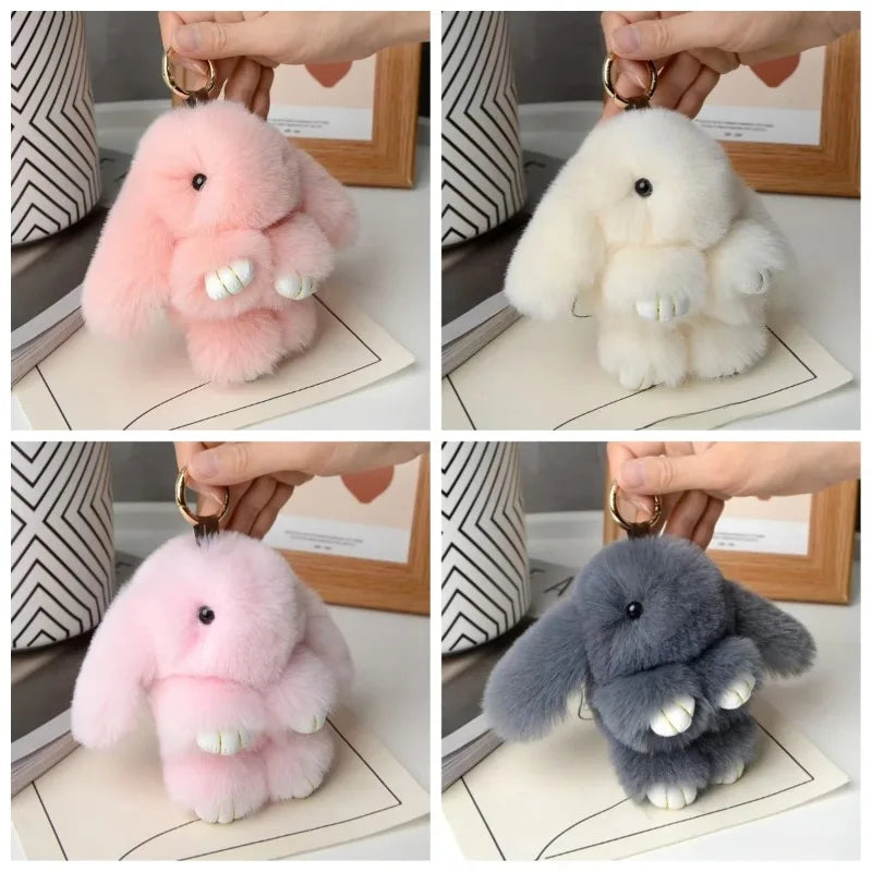 Three plush rabbit bag charms in pink, white, and gray are displayed with gold keyrings.