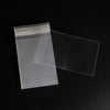 A stack of clear transparent card sleeves or protectors lying on a dark surface.