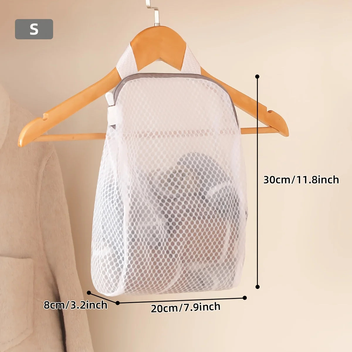 A white honeycomb mesh laundry bag is shown hanging on a wooden hanger against a light wall.