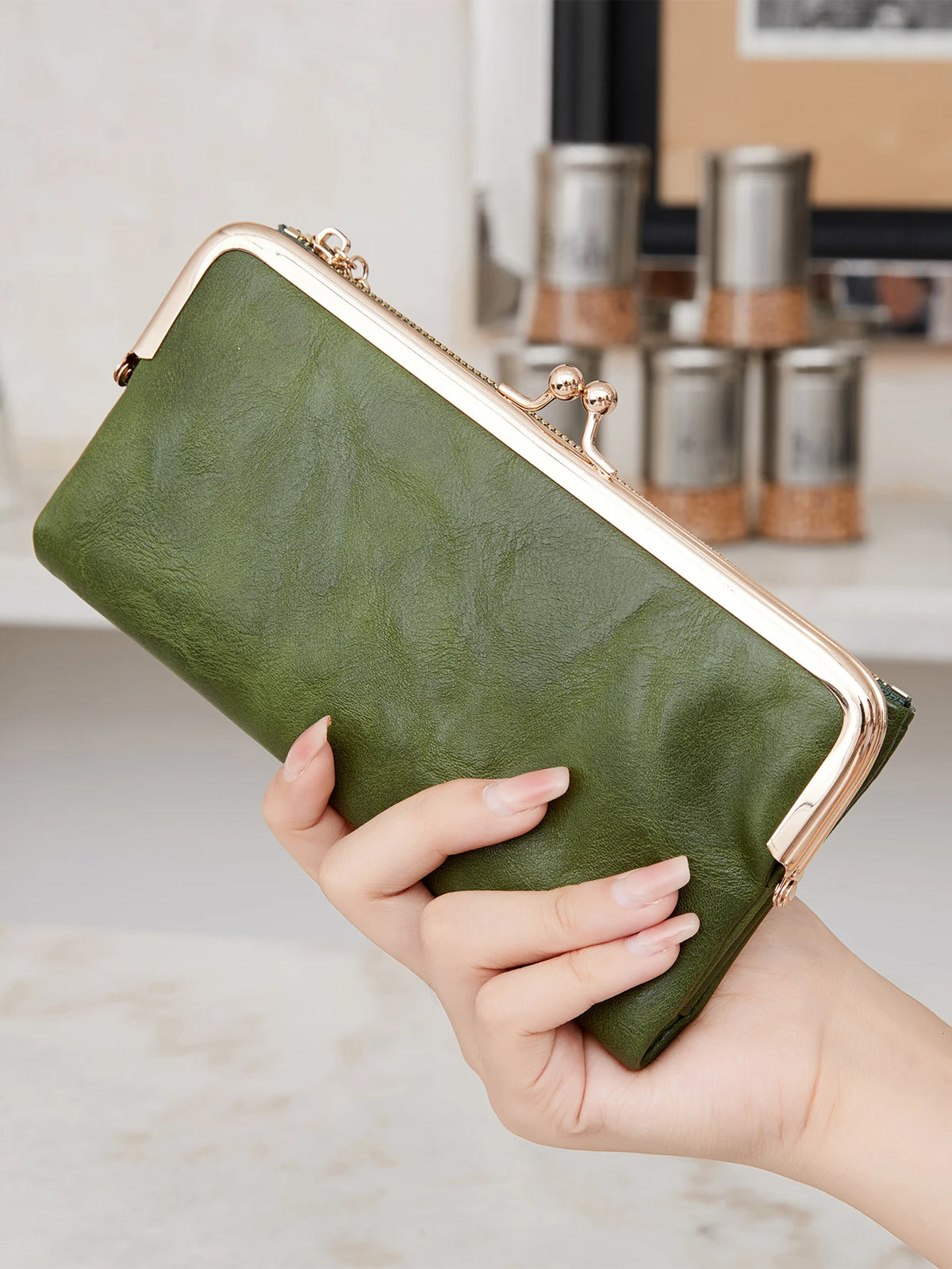 Eine Hand hält eine olivgrüne Leder-Vintage-Geldbörse mit goldenen Akzenten.