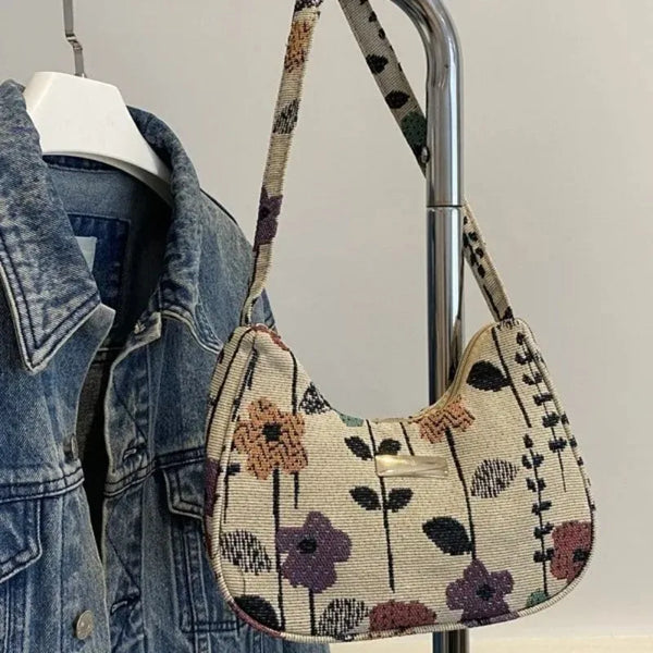 A vintage floral corduroy mini shoulder bag hanging on a metal hanger next to a denim jacket.