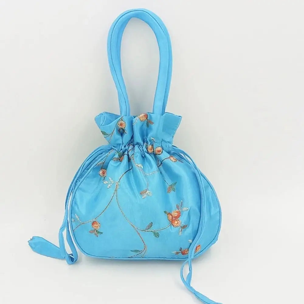 Clutch de satén azul claro con cierre de lazo decorado con bordado floral pequeño.