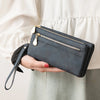 A hand holds a dark gray leather wallet with a gold zipper and a leather tag against a light colored blouse.