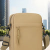 Sac bandoulière beige unisexe posé sur une surface claire avec des bâtiments de ville flous en arrière-plan.
