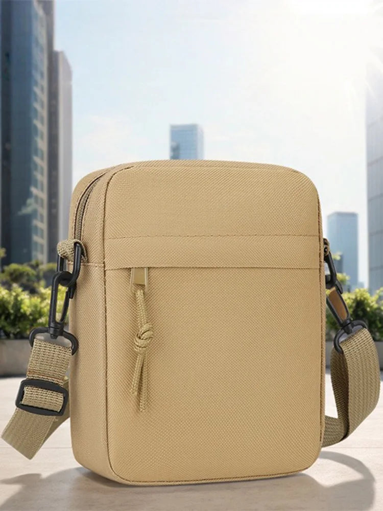 Sac bandoulière beige unisexe posé sur une surface claire avec des bâtiments de ville flous en arrière-plan.