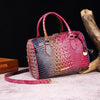 A red crocodile pattern luxury leather crossbody tote bag resting on a light surface next to a piece of driftwood.
