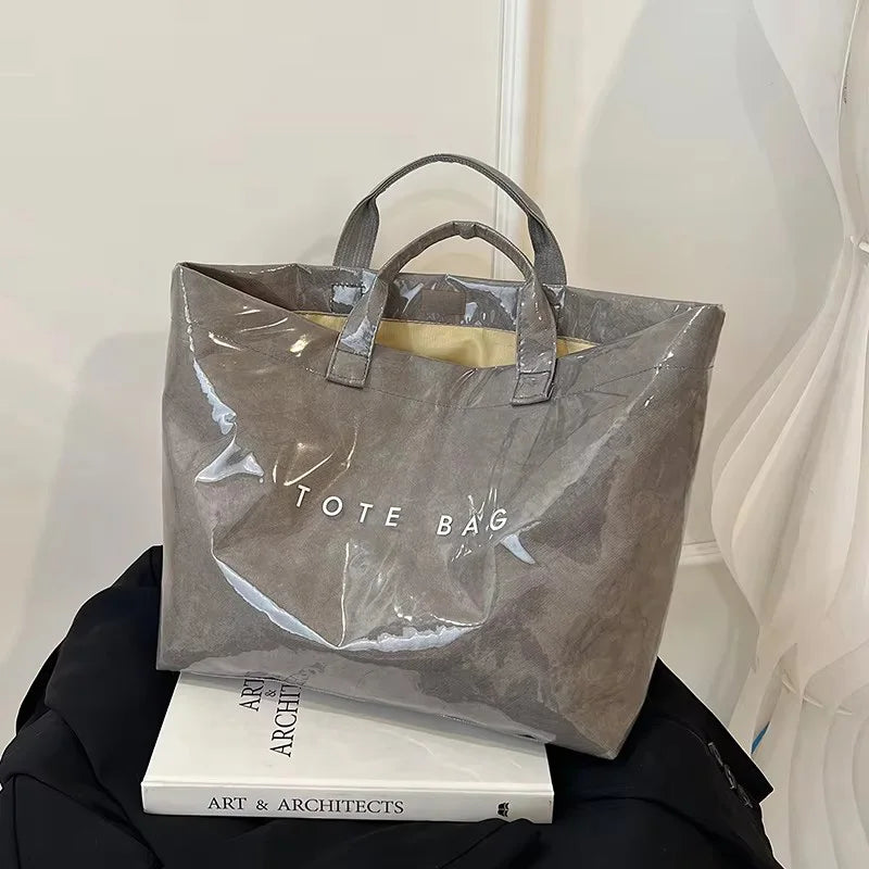 Una bolsa tote minimalista de PVC gris junto a un libro titulado Arte y Arquitectos.