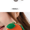 A red felt cherry-shaped coin purse keychain with a green leaf detail and several silver coins.